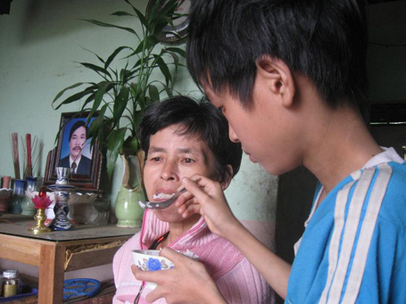  Nguyễn Sĩ Phương Anh đang bón cho mẹ ăn bên chiếc bàn thờ bố đã ọp ẹp nhưng vẫn không có tiền thay.